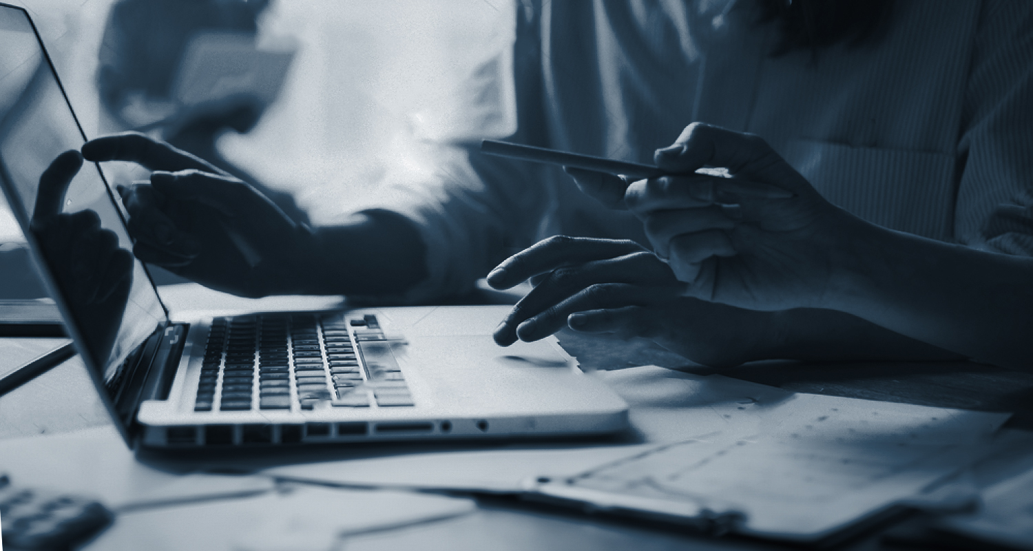Laptop met 2 personen die er naar kijken. De ene persoon wijst naar het scherm en de andere hand ligt op het muispad. De andere persoon heeft een pen vast die ook naar het scherm wijst.